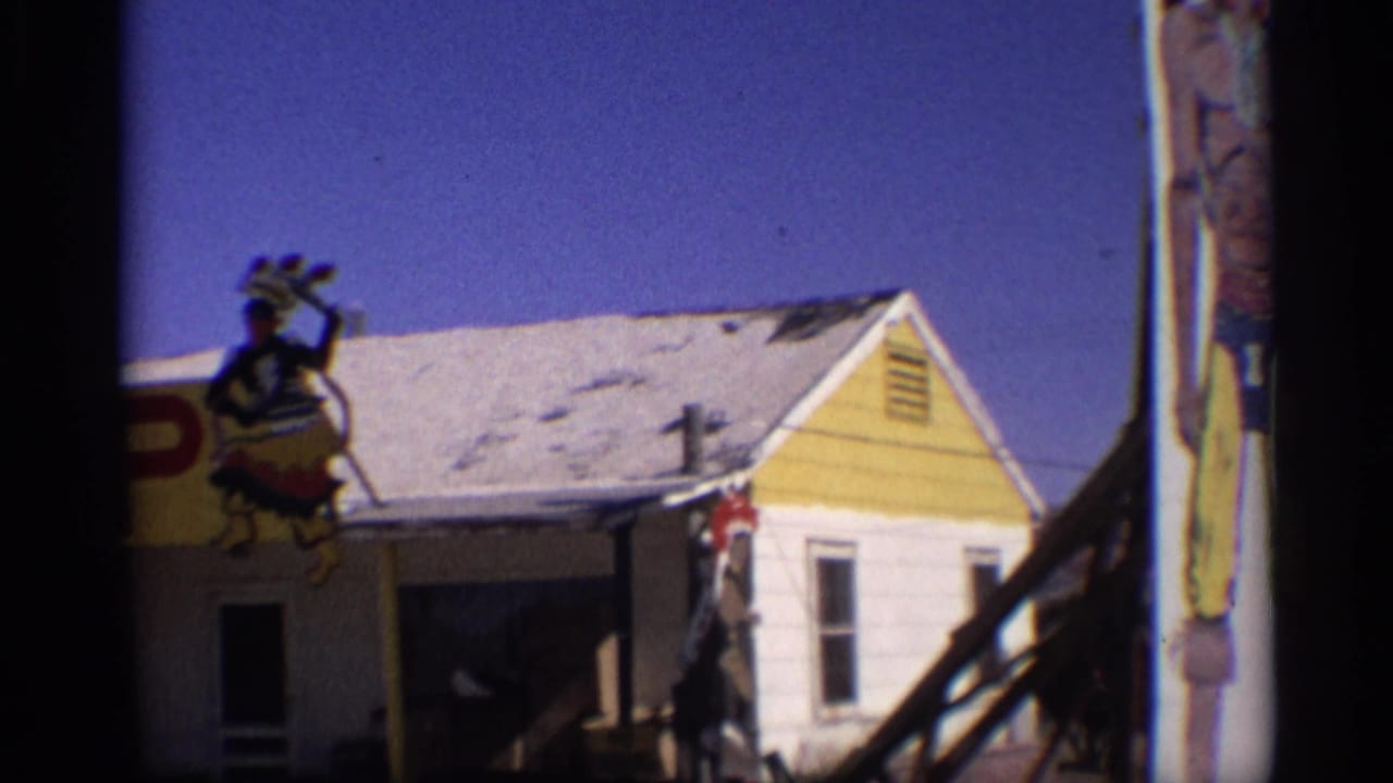 Yellow roadside building with roof-mounted figure and part of a tall painted sign at the edge.