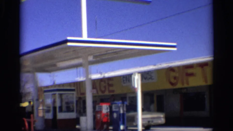 1959 Arizona roadside station view with canopy supports, gift shop lettering, pumps, entrance, and a white car near the storefront.