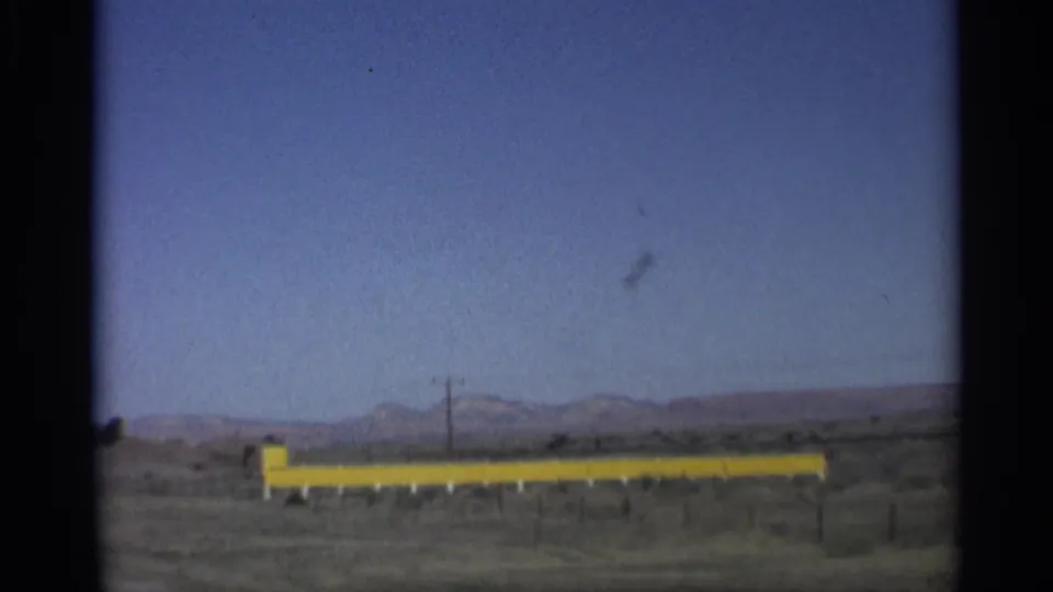 1959 Arizona road-trip frame with a bright yellow barrier, utility pole, open desert, and distant mountain ridge.