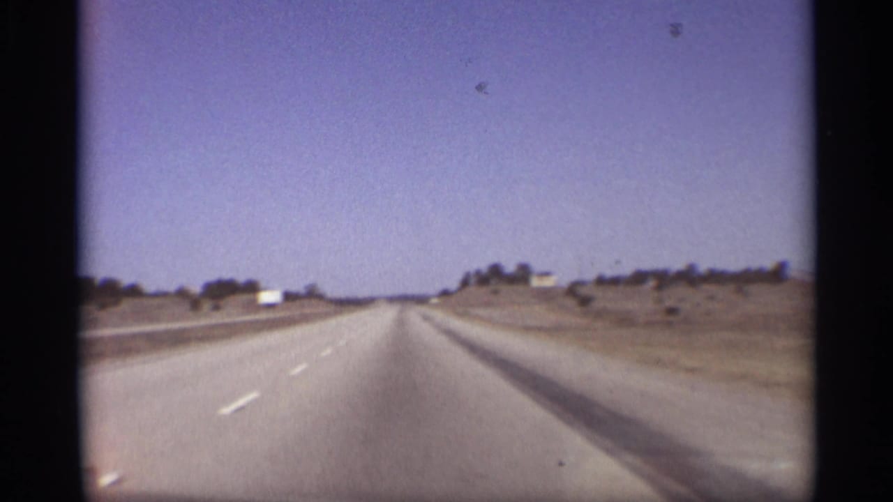 Forward view down a wide desert highway with lane markings and low roadside scrub.