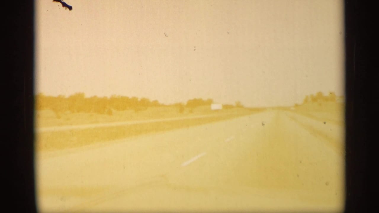 Overexposed highway view with pale road, roadside scrub, and distant horizon.
