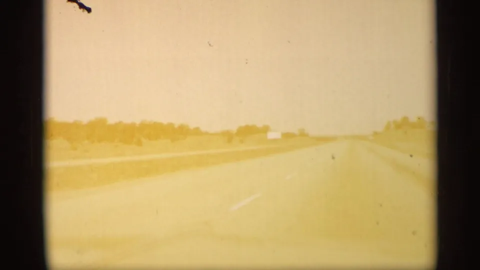 Faded 8mm frame from the Arizona road sequence, with the highway ahead partly washed by bright exposure.