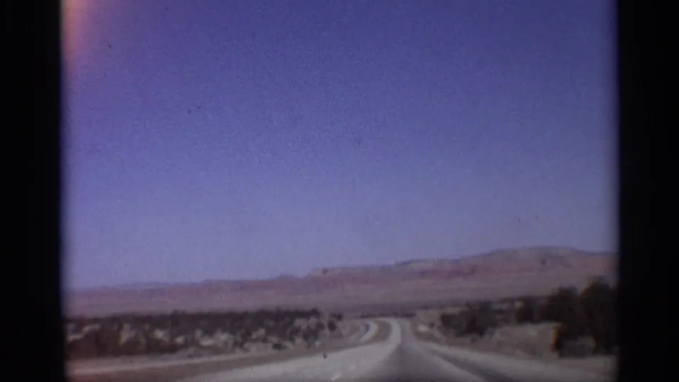 1959 Arizona road-trip frame showing a curving highway through sparse desert terrain with low hills beyond.
