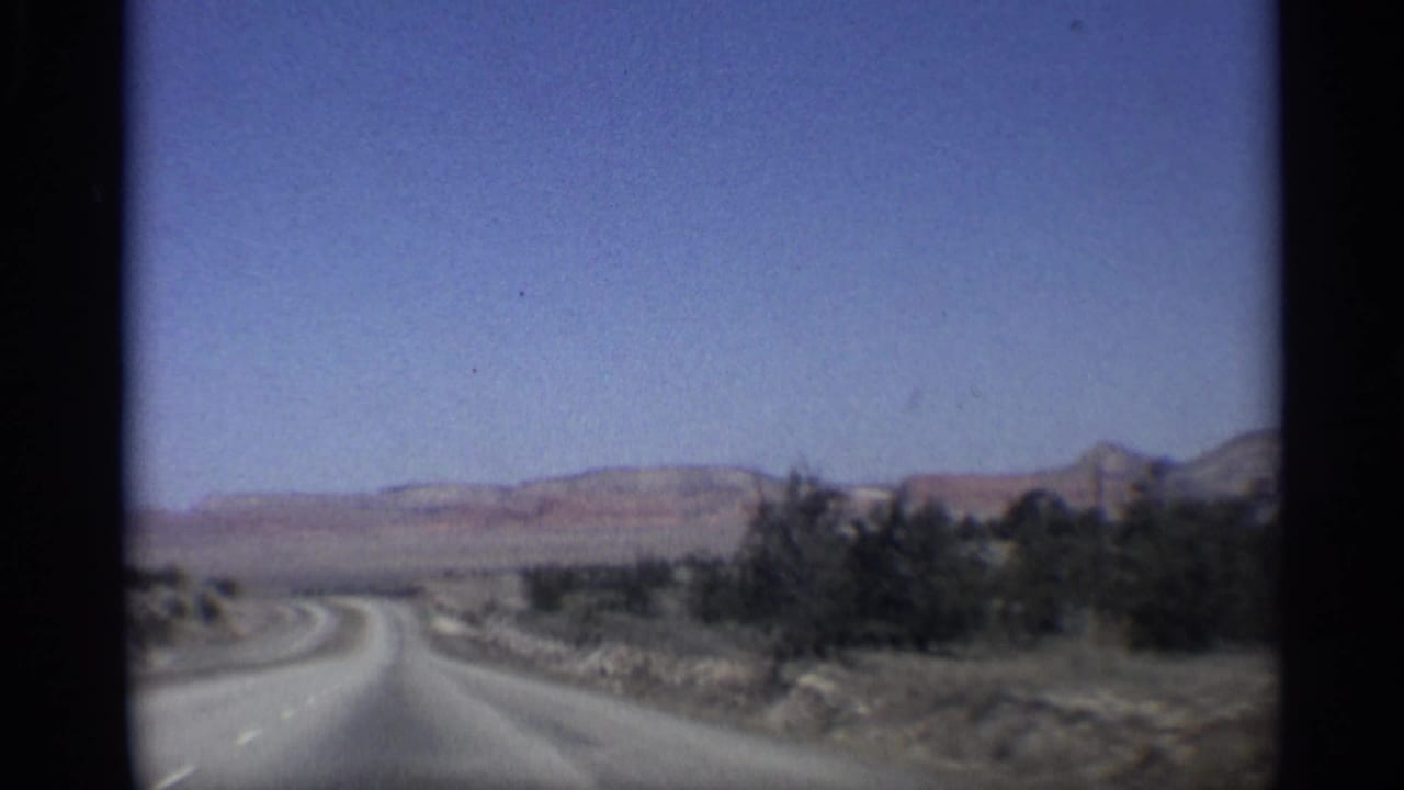 Paved highway curving through desert terrain with low hills and shrubs under blue sky.