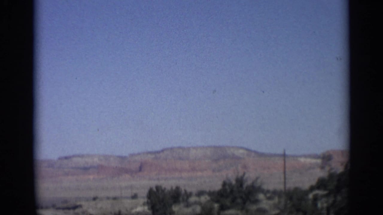 Distant desert mesas and shrubs seen from a moving roadside viewpoint.
