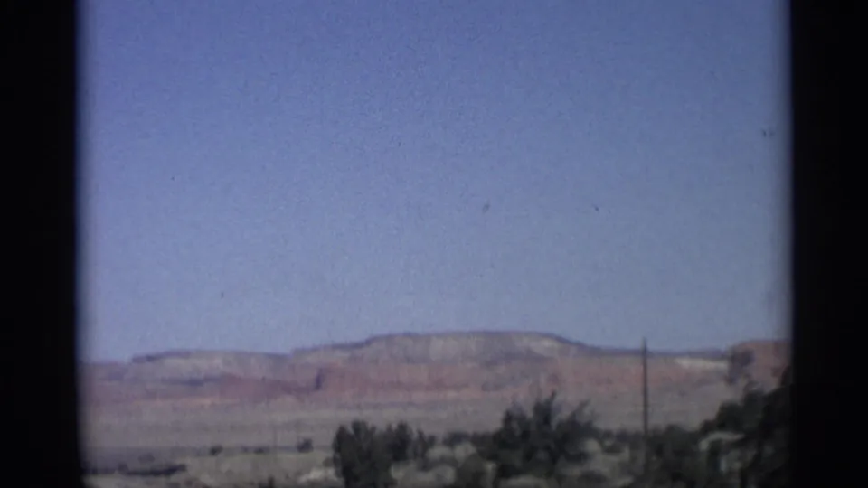 1959 Arizona 8mm frame with low mesas, sparse brush, a utility pole, and open desert beneath a blue sky.