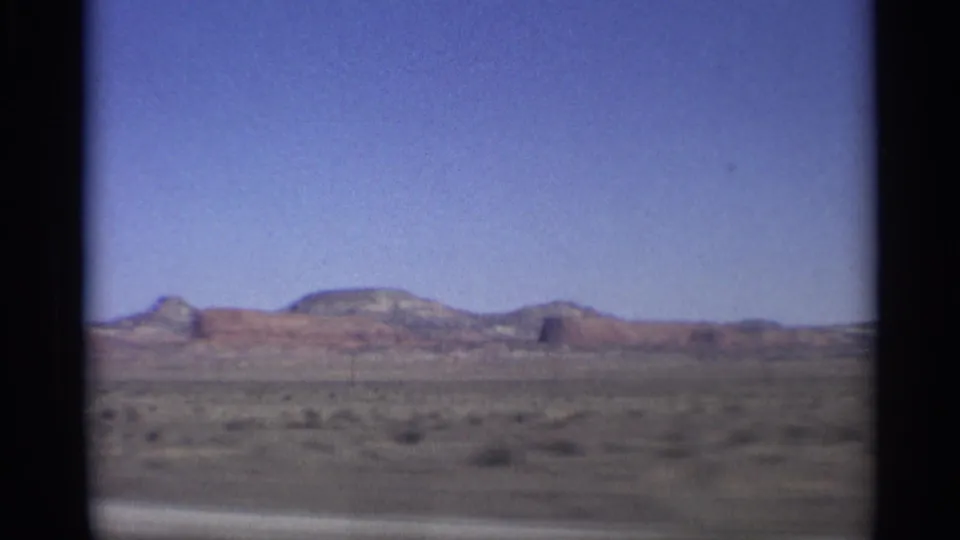 1959 Arizona home-movie view of open desert scrub and distant red rock plateaus seen from a moving vehicle.