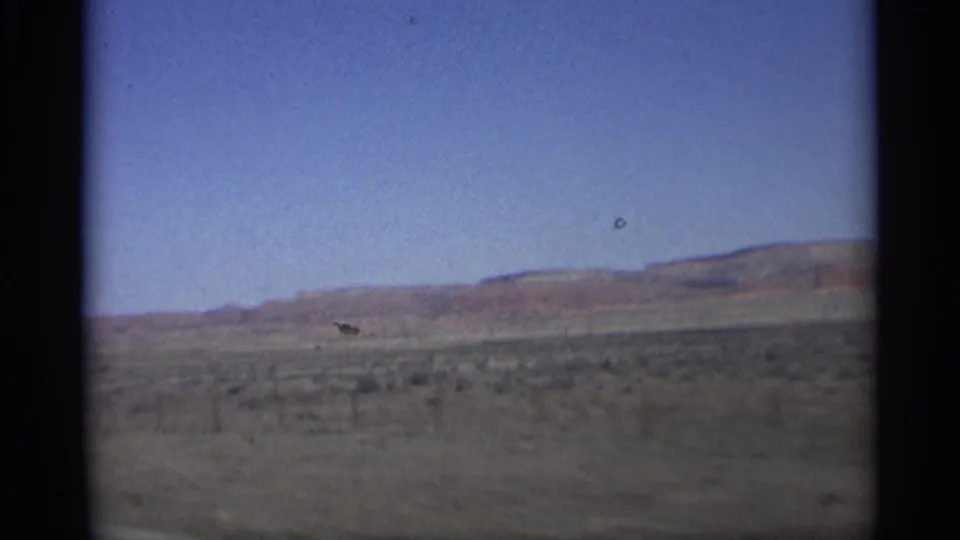 Moving 8mm view across Arizona desert terrain with a low red ridge and sparse vegetation on the plain.