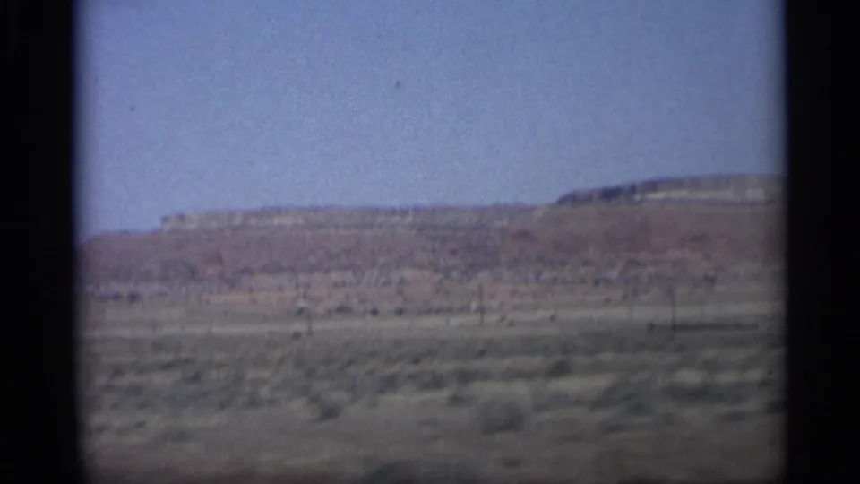 Arizona desert scene from a moving vehicle, showing scrubland, a distant mesa, and soft 8mm motion blur.