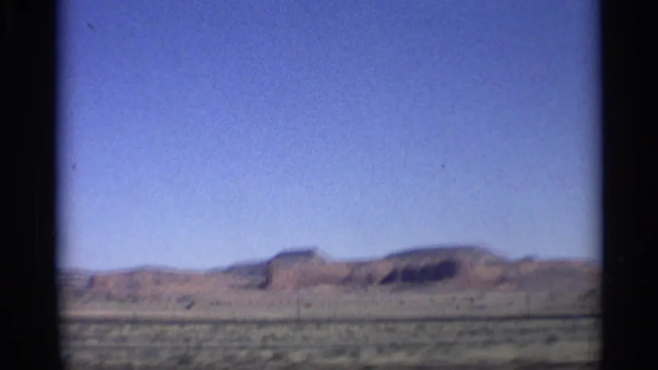 1959 Arizona 8mm frame with a red rock butte on the horizon and open desert scrub in the foreground.