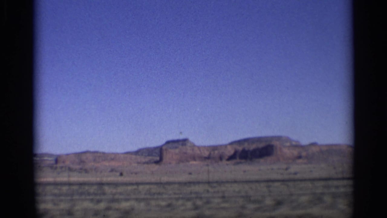 Distant mesa and desert plain under blue sky, seen through dark film gate edges.