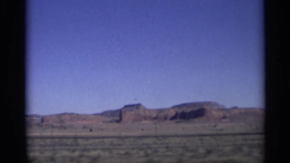 1959 Arizona 8mm frame showing a distant mesa across a flat desert plain beneath a clear blue sky.