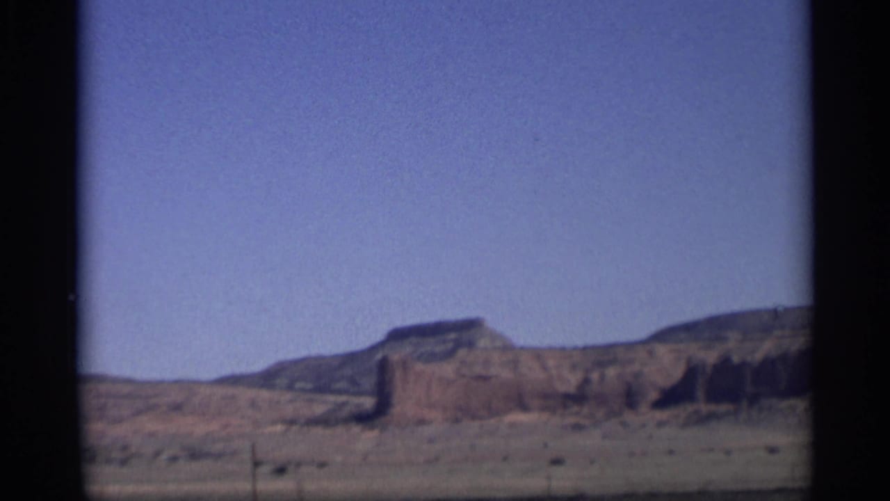 Broad desert landscape with mesa formations and open sky, framed by film borders.