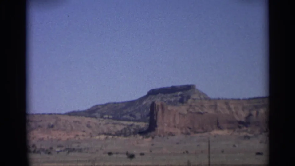 1959 Arizona 8mm view of a mesa wall, arid foreground, and roadside utility pole from a moving vehicle.