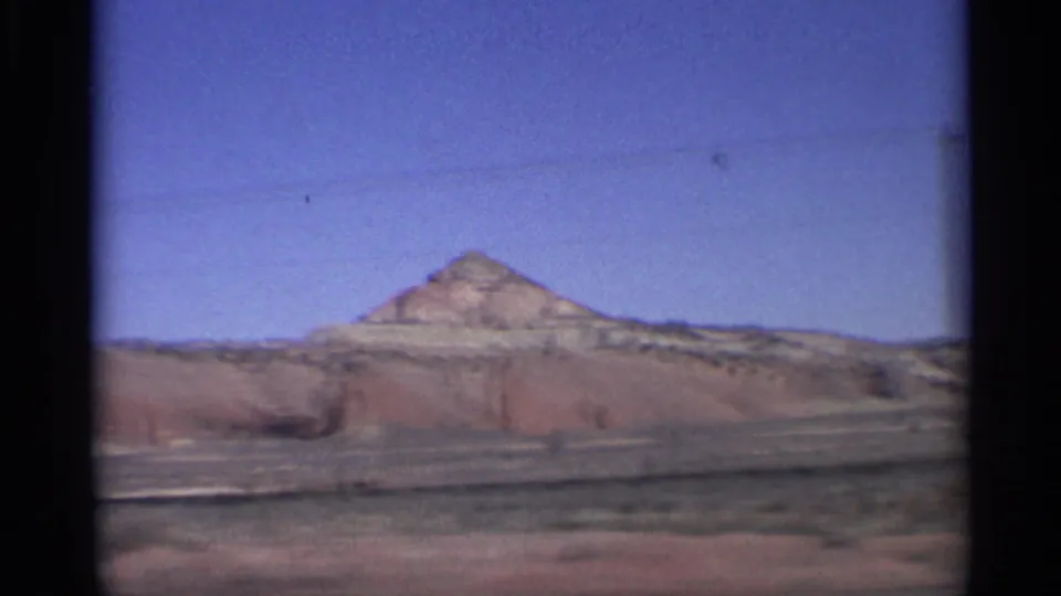 1959 Arizona 8mm frame showing a pyramid-like desert hill beyond layered arid terrain and open sky.