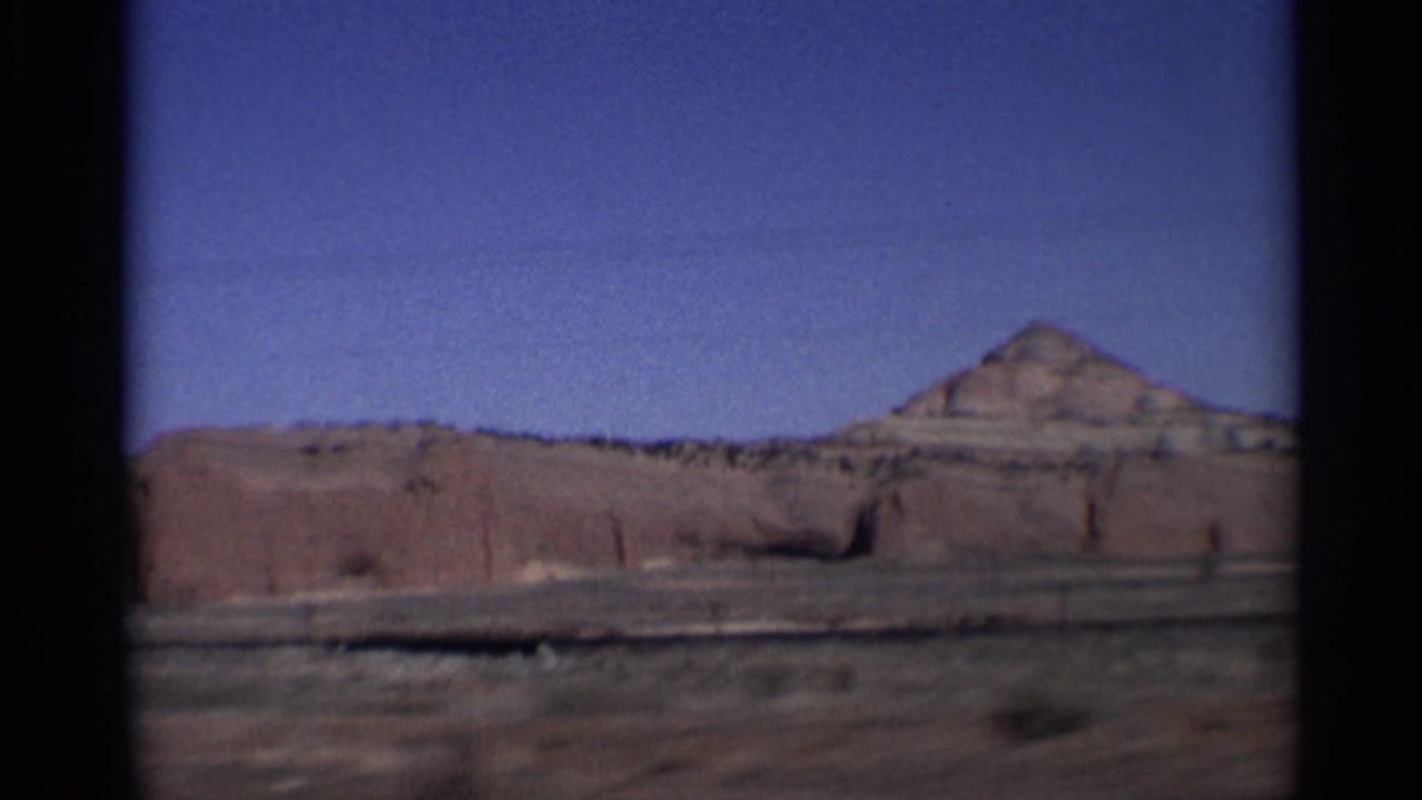 Red rock desert formation beyond a road edge under a clear blue sky.
