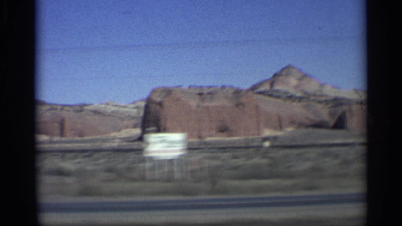 Large red rock formation with a roadside sign in the foreground.