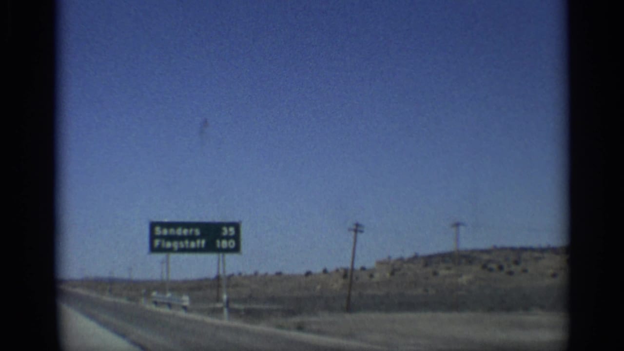 Highway sign beside an Arizona desert road lists Sanders 35 and Flagstaff 180.