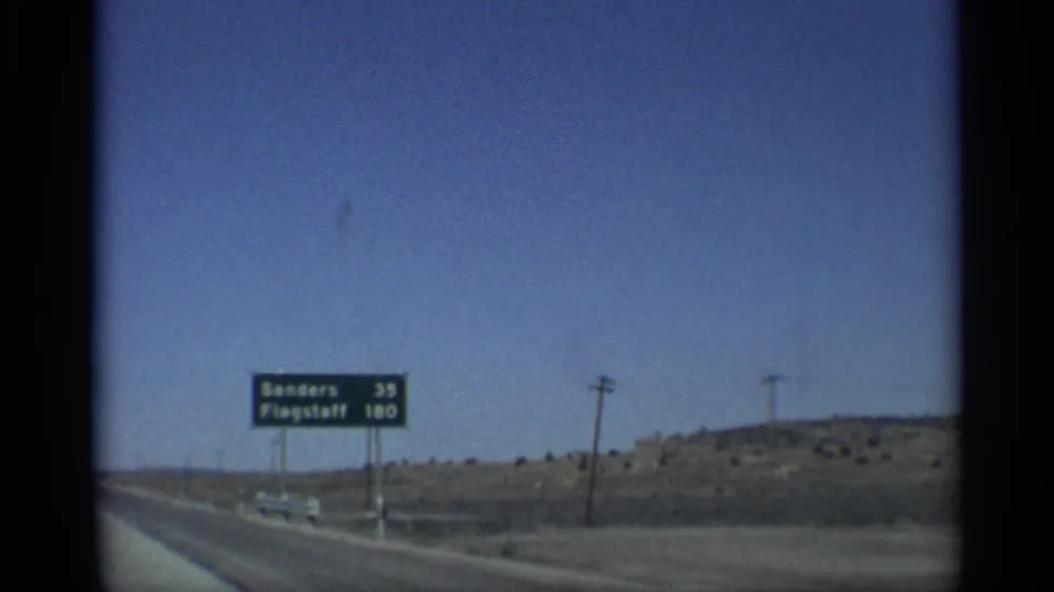 1959 Arizona 8mm road footage showing a green distance sign for Sanders and Flagstaff beside a desert highway.