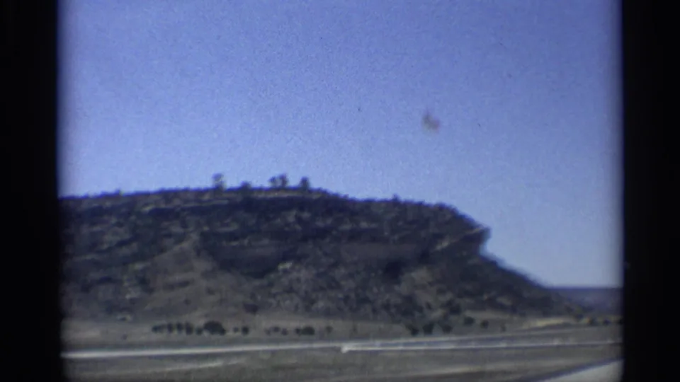 1959 Arizona desert landscape with a rocky hill, sparse vegetation, roadway edge, and soft 8mm framing.