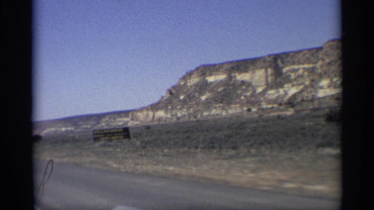 1959 Arizona 8mm frame showing a roadside view of arid hills, scrub, and open sky from a moving car.