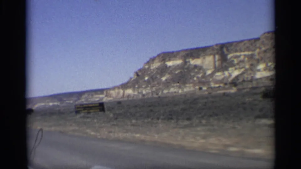 1959 Arizona 8mm frame showing a roadside view of arid hills, scrub, and open sky from a moving car.