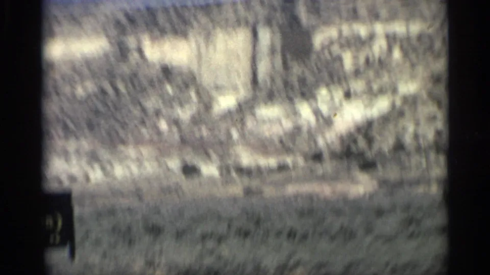 1959 Arizona frame with a blurred roadside sign area against pale desert hills, softened by motion and film grain.