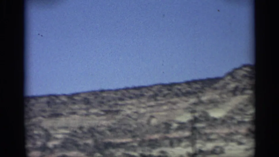 1959 Arizona home-movie frame showing a scrub-covered desert hillside beneath a clear blue sky.