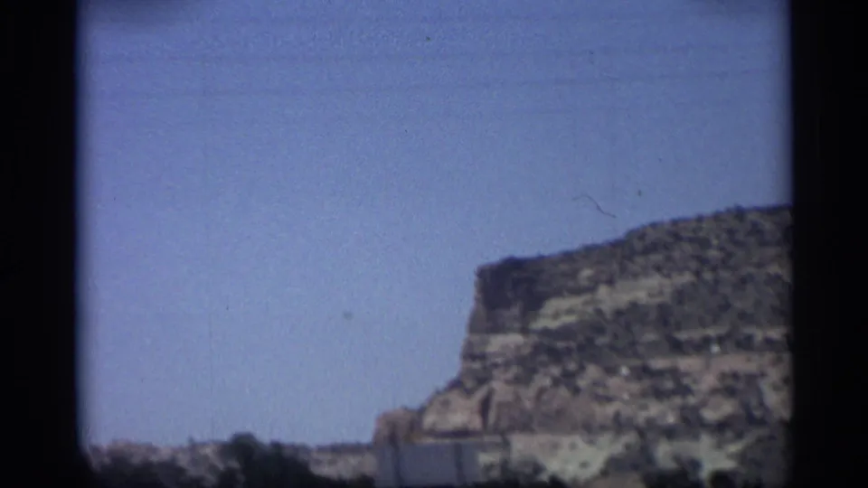 1959 Arizona travel footage frame with a flat-topped bluff, sparse vegetation, and open blue sky.