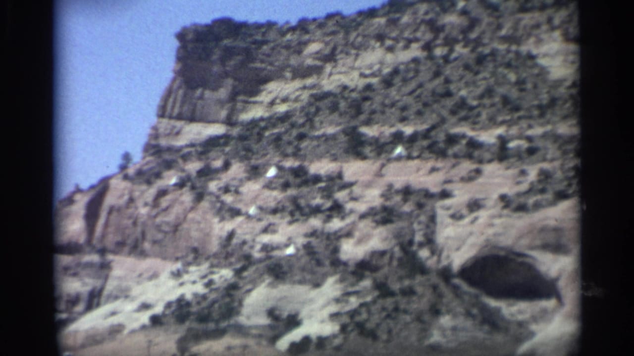 Layered canyon wall under blue sky with a dark cave opening near the lower right.
