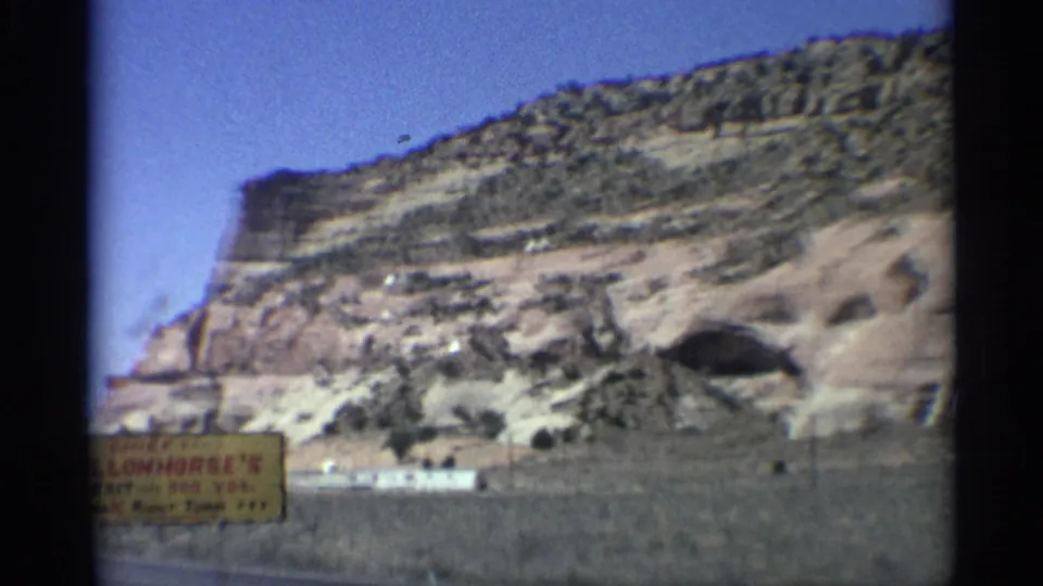 1959 Arizona roadside frame showing layered canyon rock, cave opening, road edge, and a Chief Yellowhorse sign.