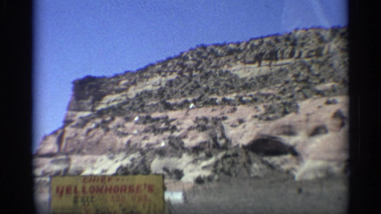 Layered desert cliff with a yellow Chief Yellowhorse roadside sign in the foreground.