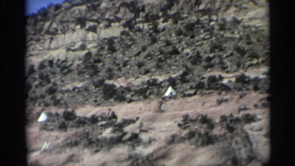 Visitor-shot Arizona desert view with white tents, low shrubs, and a layered cliff face in the background.