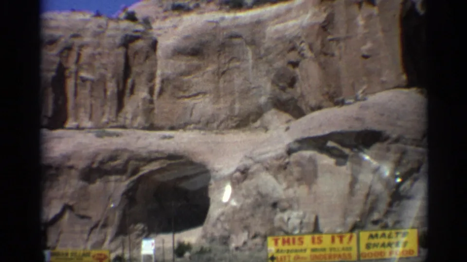 Arizona roadside rock formation with a large cave-like opening, weathered cliff walls, and yellow signs near the foreground.