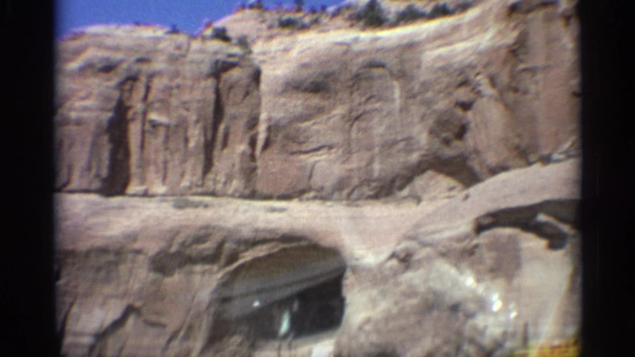 Sandstone cliff with a dark rock arch opening and a vehicle partly visible at the lower edge.