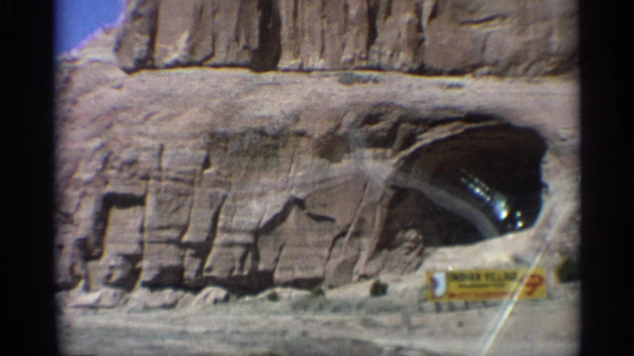Rock arch or tunnel-like opening in sandstone with a small roadside sign near the road.