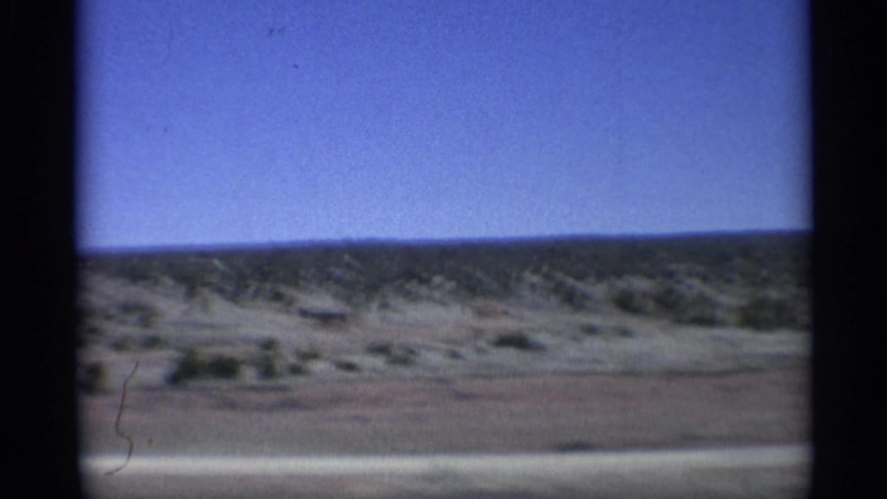 Desert scrubland and distant low hills seen through dark 8mm frame edges.