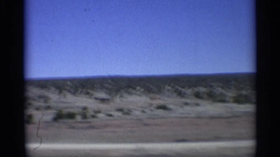 1959 Arizona road-view frame showing arid scrubland, a distant ridge, and clear blue sky through visible film gate edges.