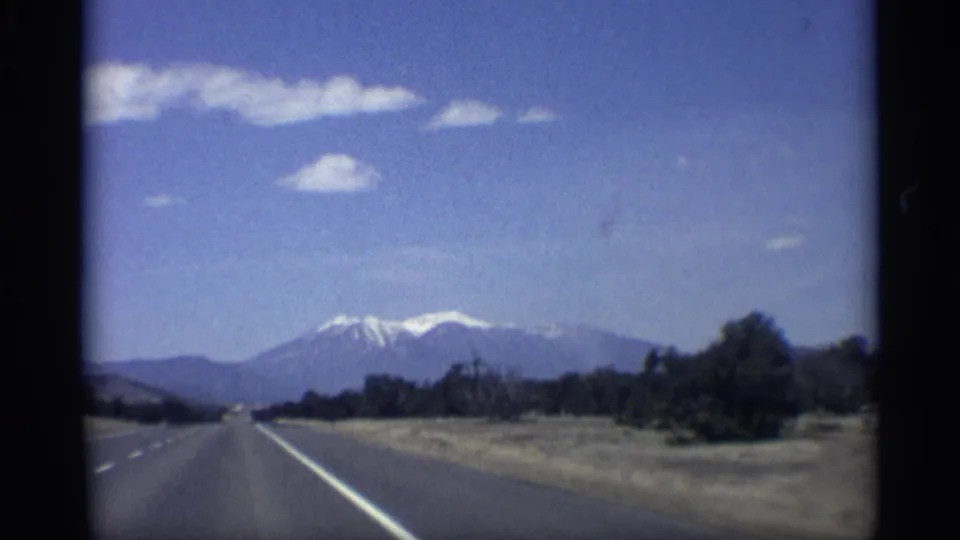1959 Arizona travel shot looking down an open highway toward distant snow-capped mountains under a blue sky.