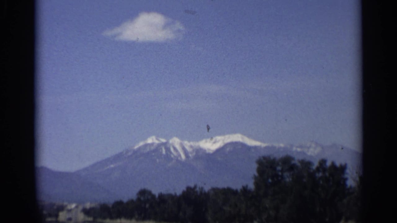 Distant snow-capped peaks with trees below and a small cloud overhead.