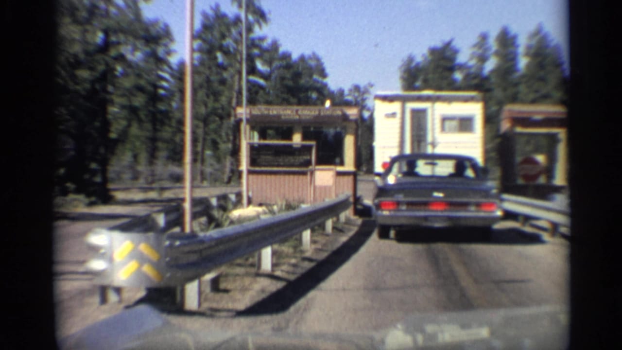 Dark sedan waits behind a camper trailer at a forested ranger station entrance.