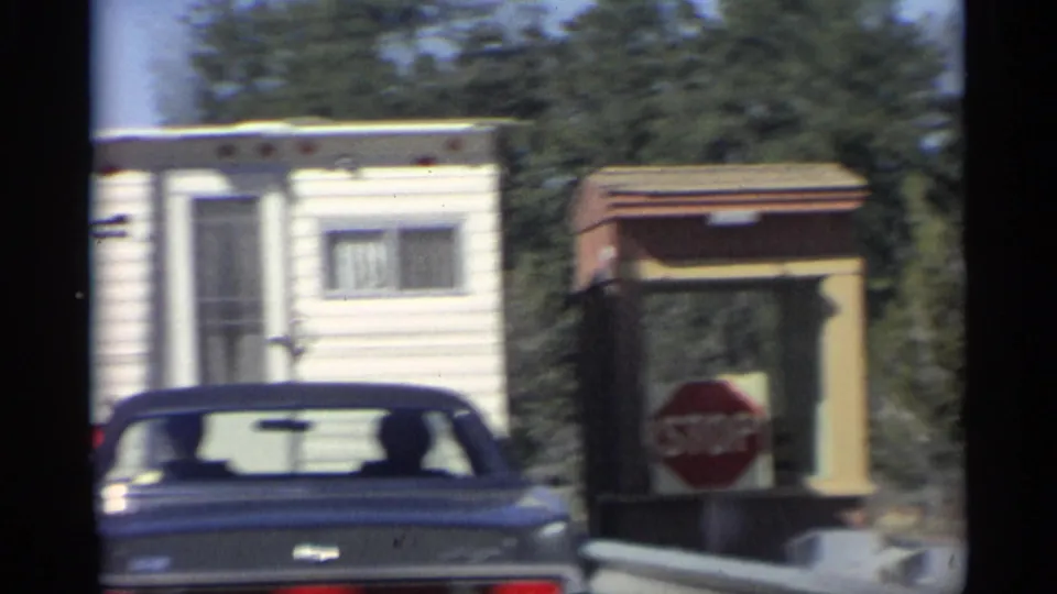 1959 Arizona frame showing the rear of a dark sedan near a camper trailer and stop sign at the South Entrance Ranger Station.