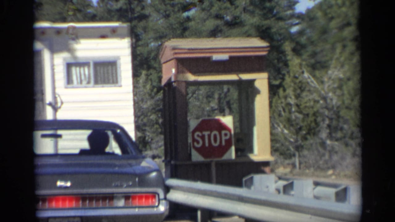 Car stopped near a stop sign and small roadside structure with trees behind it.