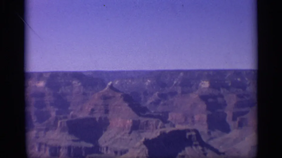 Aged 8mm view of the Grand Canyon landscape in Arizona, with layered rock formations below a clear sky.