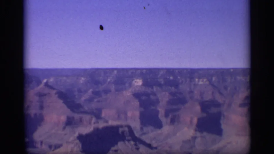 1959 8mm home-movie frame of the Grand Canyon from a high vantage point, showing distant ridges and canyon walls.