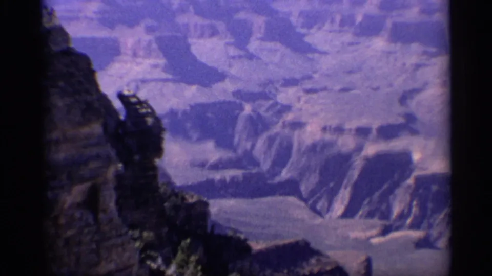 Grand Canyon overlook view on aged 8mm film, with a dark foreground cliff edge framing distant canyon formations.
