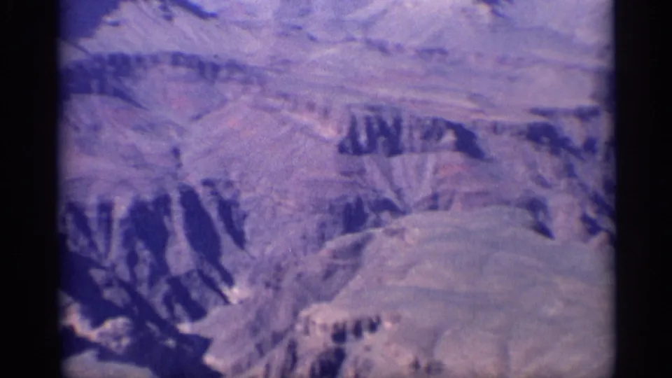 1959 Arizona aerial view over Grand Canyon ridges and layered cliff formations, softened by 8mm grain and color fading.