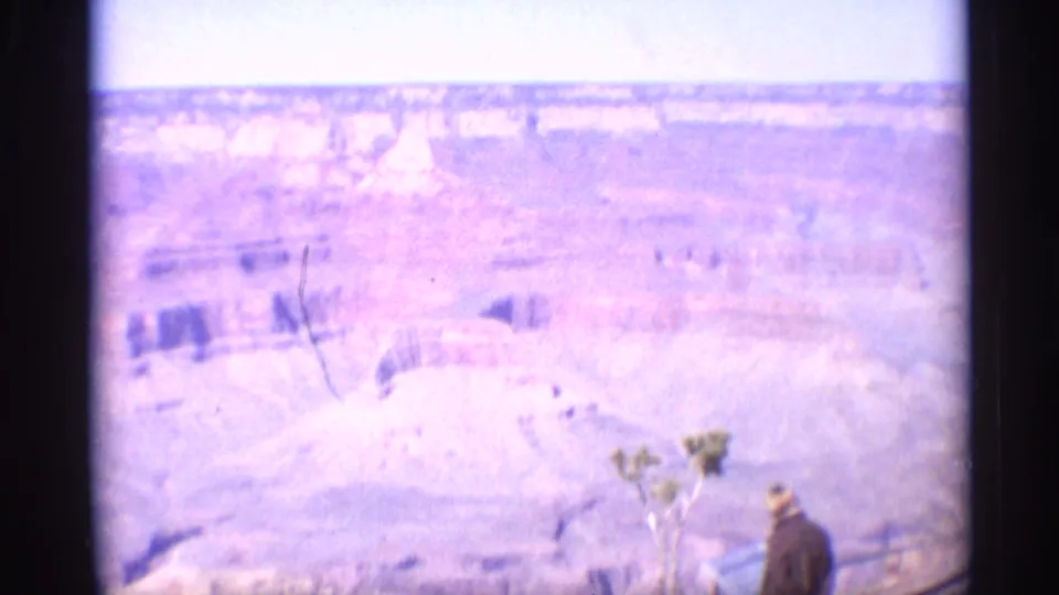 1959 Arizona home-movie view across the Grand Canyon with a visitor partly visible near the lower edge by a lookout railing.