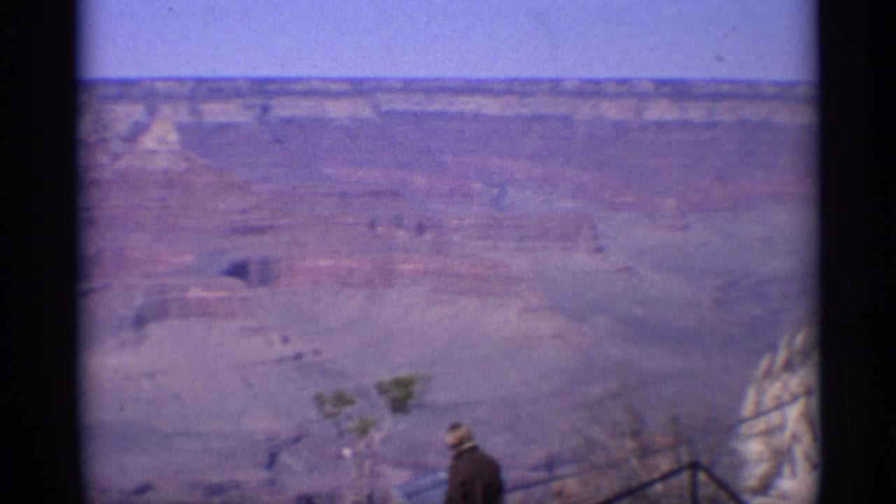 Faded 8mm view from an Arizona Grand Canyon lookout, with a visitor near railings in front of layered canyon terrain.