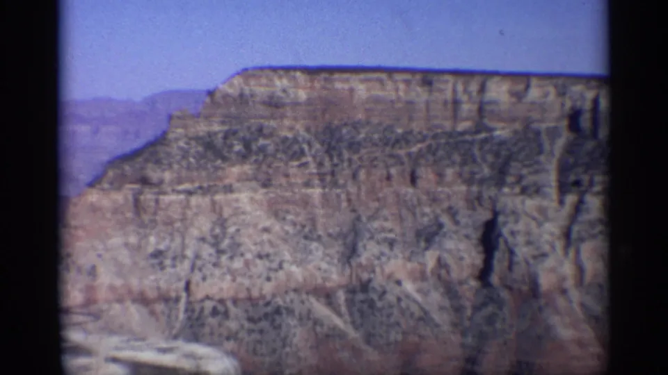 1959 Arizona 8mm frame focused on a stratified canyon cliff face, with blue sky and dark film border visible.